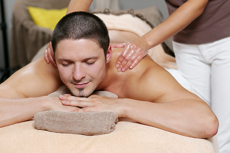 Handsome man is lying on the couch while being massaged at a spa salon