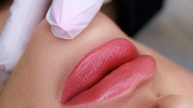 close-up of a permanent make-up of lips made in powder technique, a master in white gloves holds the lips of a model with his fingers